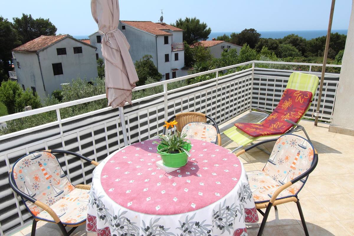 A balcony with a table, chairs, and a potted plant.