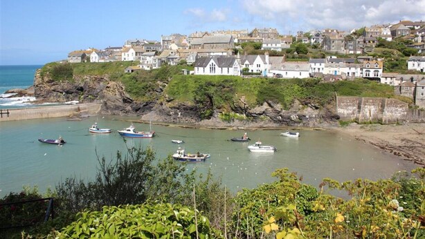 A coastal town with houses along the cliffside, boats in the water, and a view of the sea.
