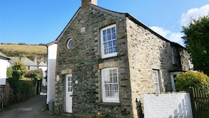 A stone building with a pitched roof, two windows, and a chimney.