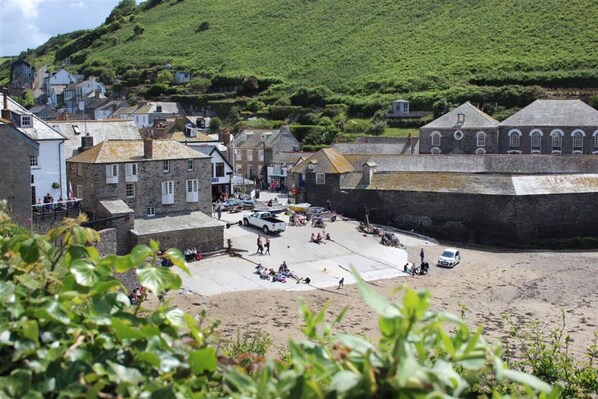 A coastal town with stone buildings, a sandy beach, and a hill in the background.