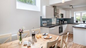 A modern kitchen with white cabinets, a wooden dining table, and a view of greenery outside. - The Organ Loft - Two Bedroom Cottage, Sleeps 4 (England)