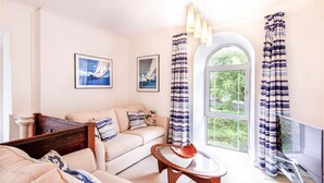 A living room with a sofa, a coffee table, and a window with curtains. There are two framed pictures on the wall. - The Organ Loft - Two Bedroom Cottage, Sleeps 4 (England)