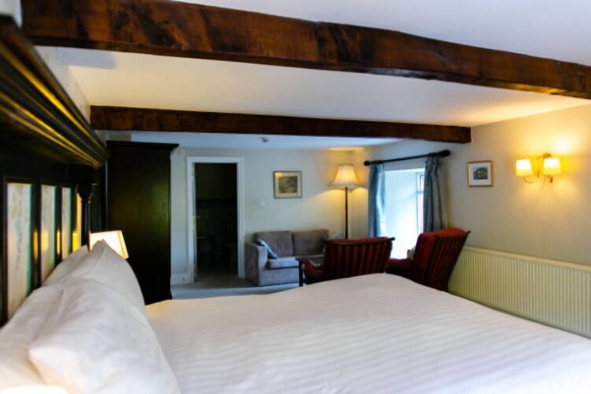 A hotel room with a large bed, a small seating area, and a view of the hallway.