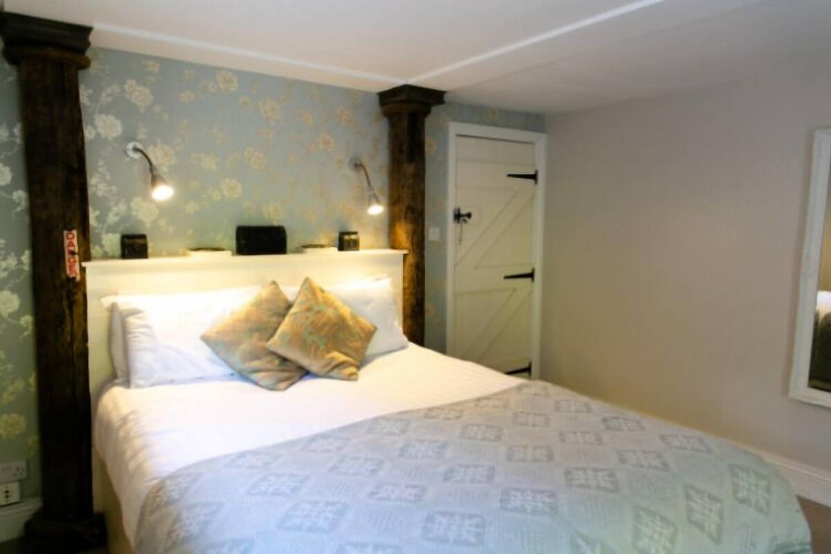 A bedroom with a bed, two wall-mounted lamps, a door, and a floral wallpaper pattern.