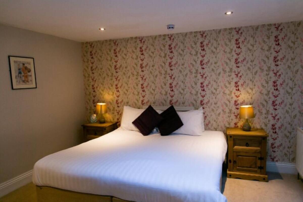 A neatly made bed with two pillows, a floral wallpaper, and two bedside lamps.