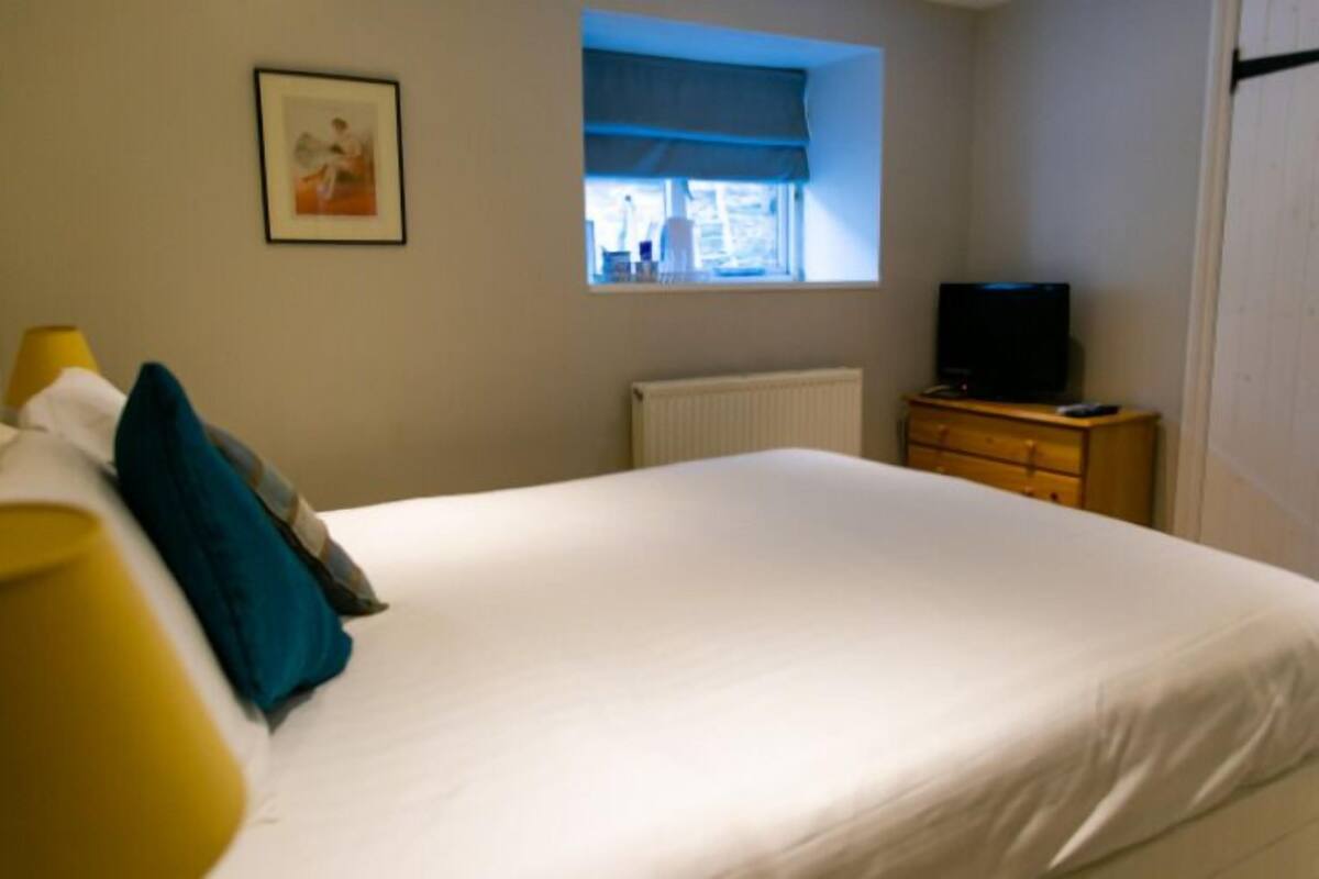 A bedroom with a bed, a window with a view, a television on a wooden dresser, and a framed picture on the wall.