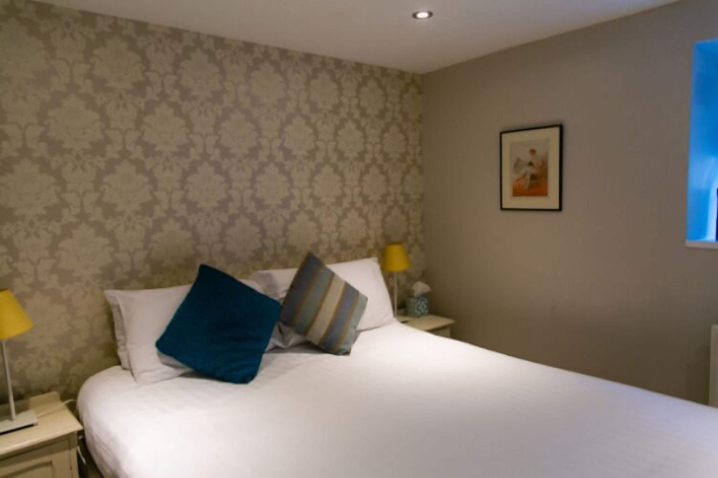 Habitación de hotel con cama, dos mesitas de noche, una lámpara y un cuadro en la pared.