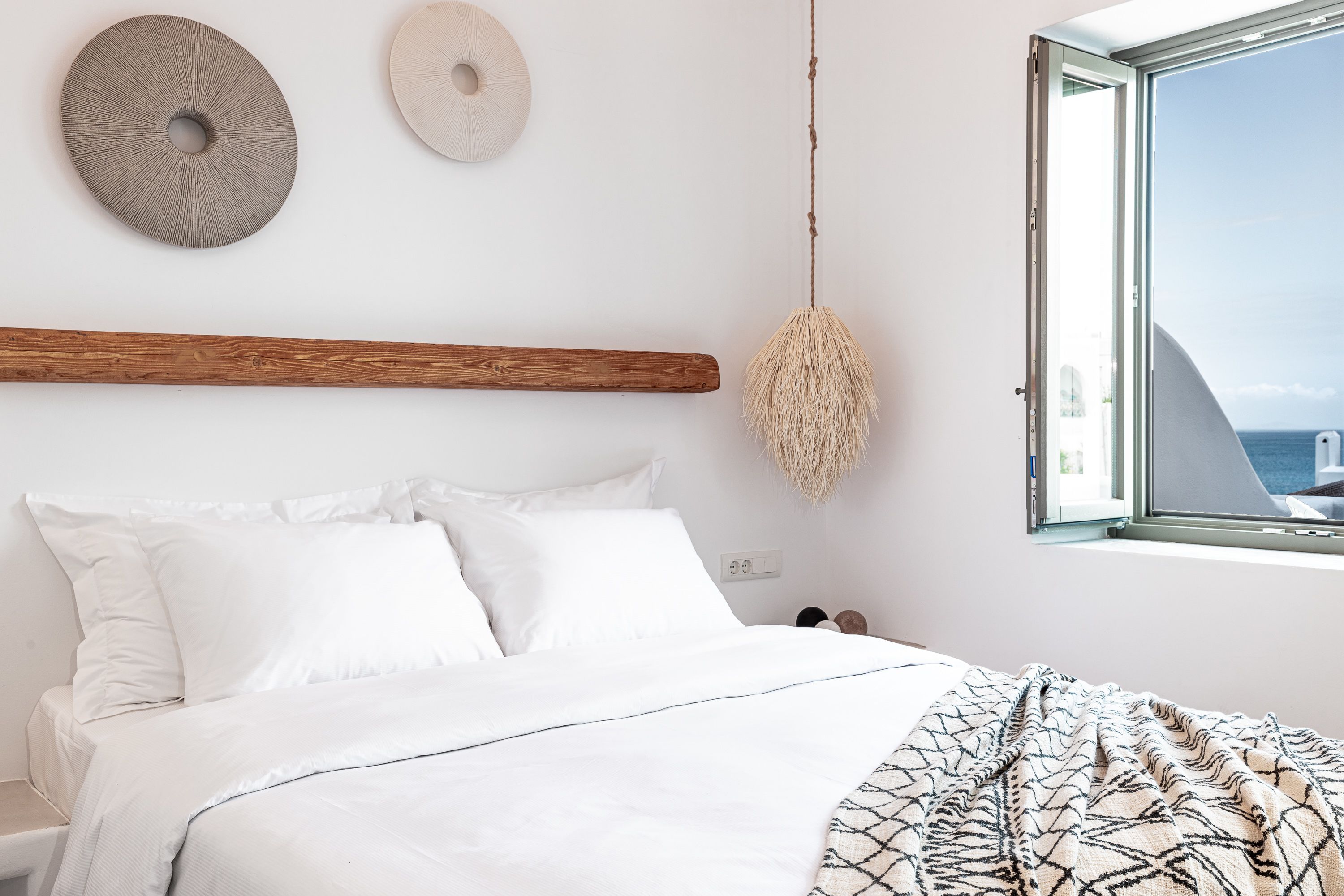 Ein Schlafzimmer mit einem Bett, weißer Bettwäsche, einem Holz-Kopfteil, einer Pendelleuchte und einem Fenster mit Blick.