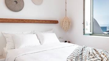 Ein Schlafzimmer mit einem Bett, weißer Bettwäsche, einem Holz-Kopfteil, einer Pendelleuchte und einem Fenster mit Blick.