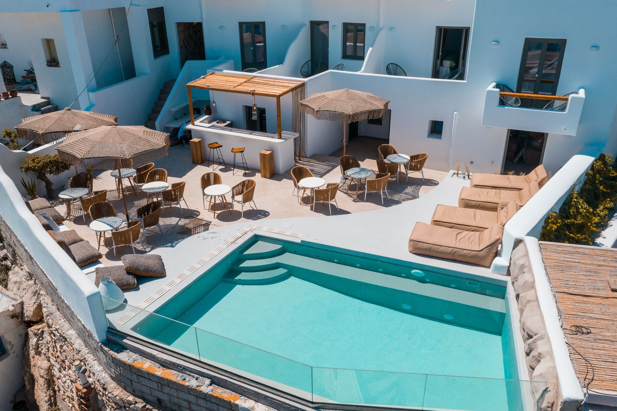 Uma área de piscina no terraço com espreguiçadeiras e guarda-sóis, rodeada por edifícios brancos.