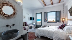 A modern bedroom with a large bed, a built-in sink, a television, and a view of the sea through an open door. - Bohemian Luxury Boutique Hotel - Adults Only (Paros)