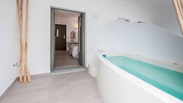 Un baño moderno con bañera, zona de ducha y puerta que da a un dormitorio.