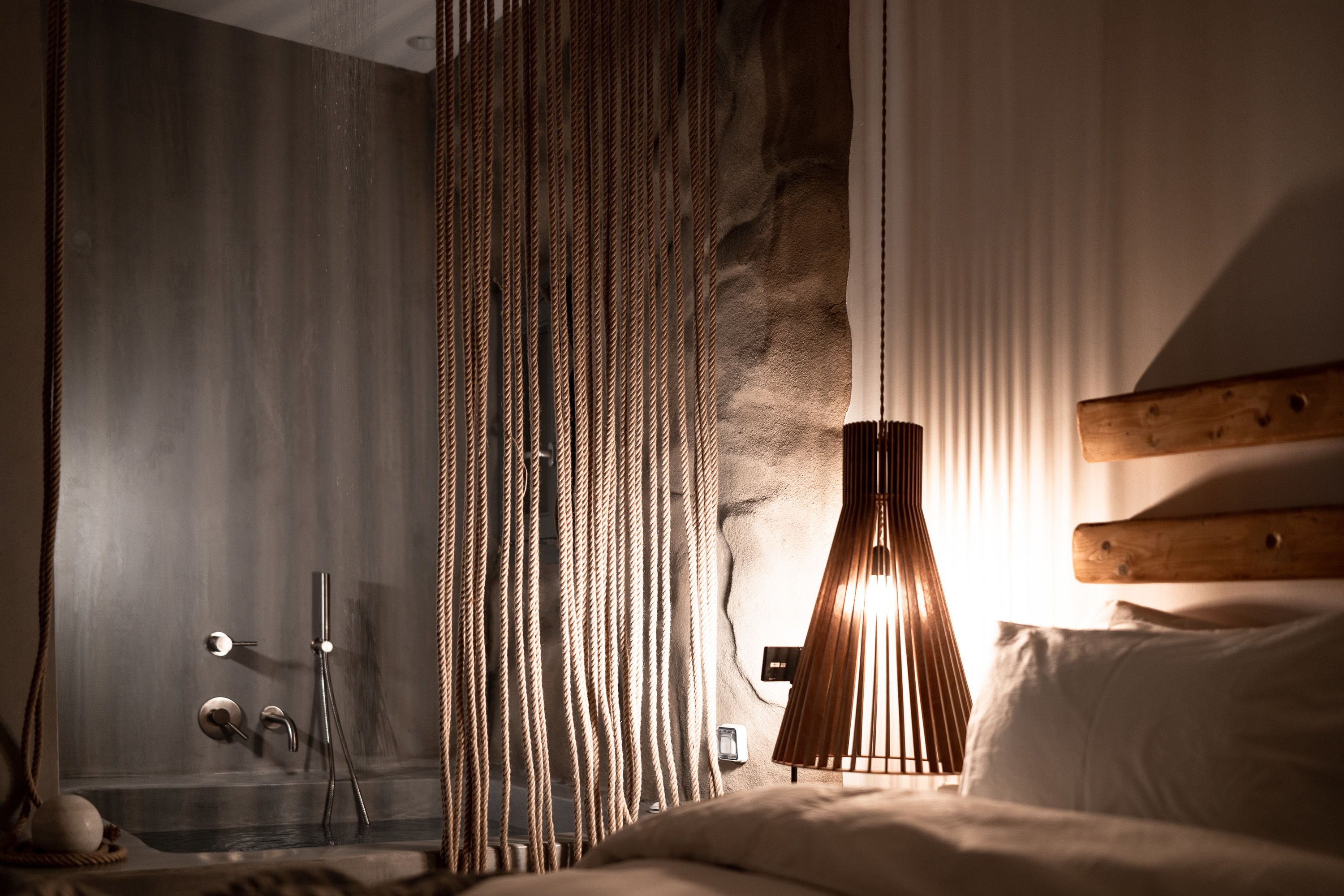 A bedroom with a bed, a bedside lamp, a wooden headboard, and a curtain.