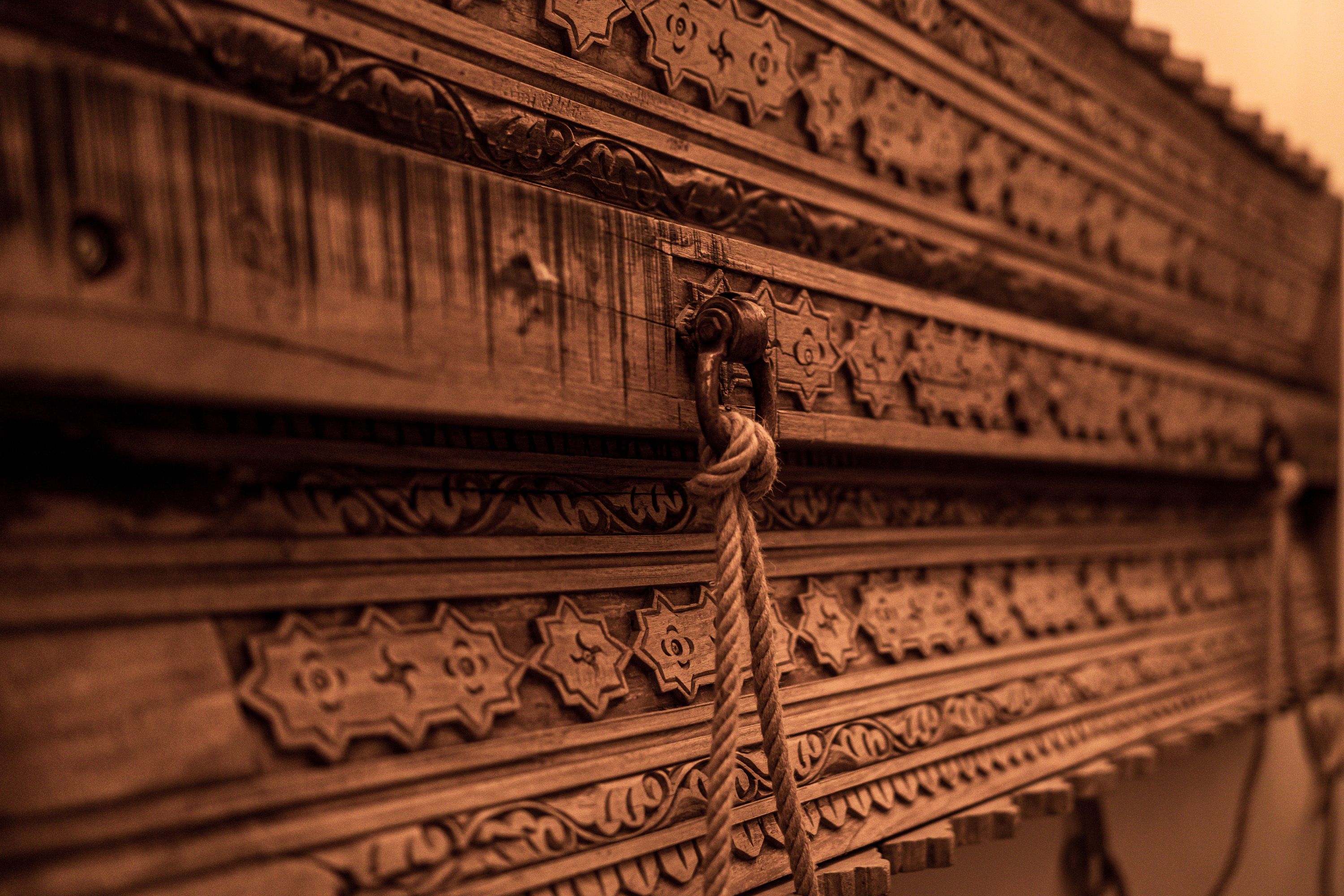 A close-up of a wooden surface with intricate carvings and a rope tied to a hook.
