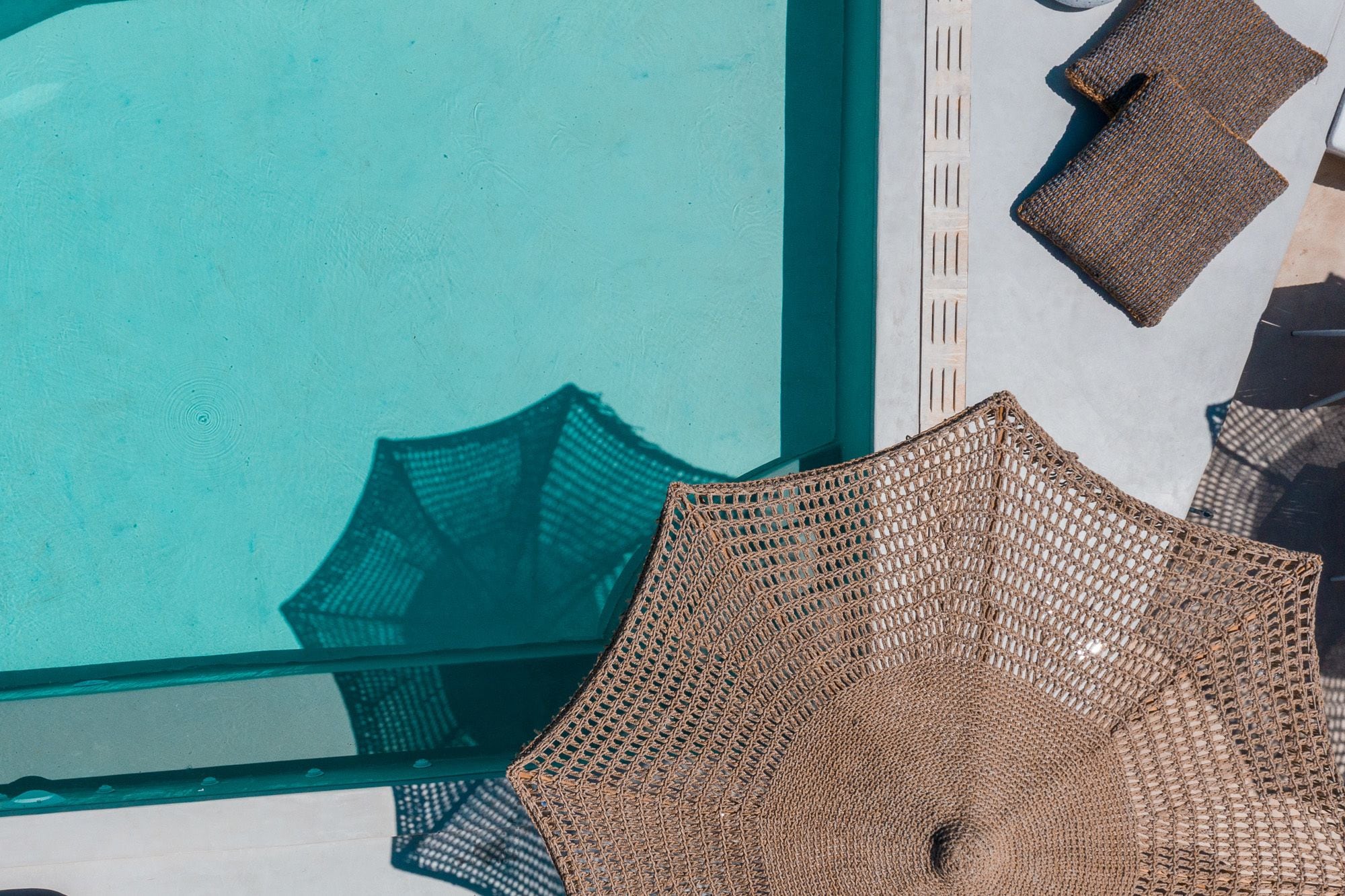 A poolside view with a woven mat and a wooden structure.