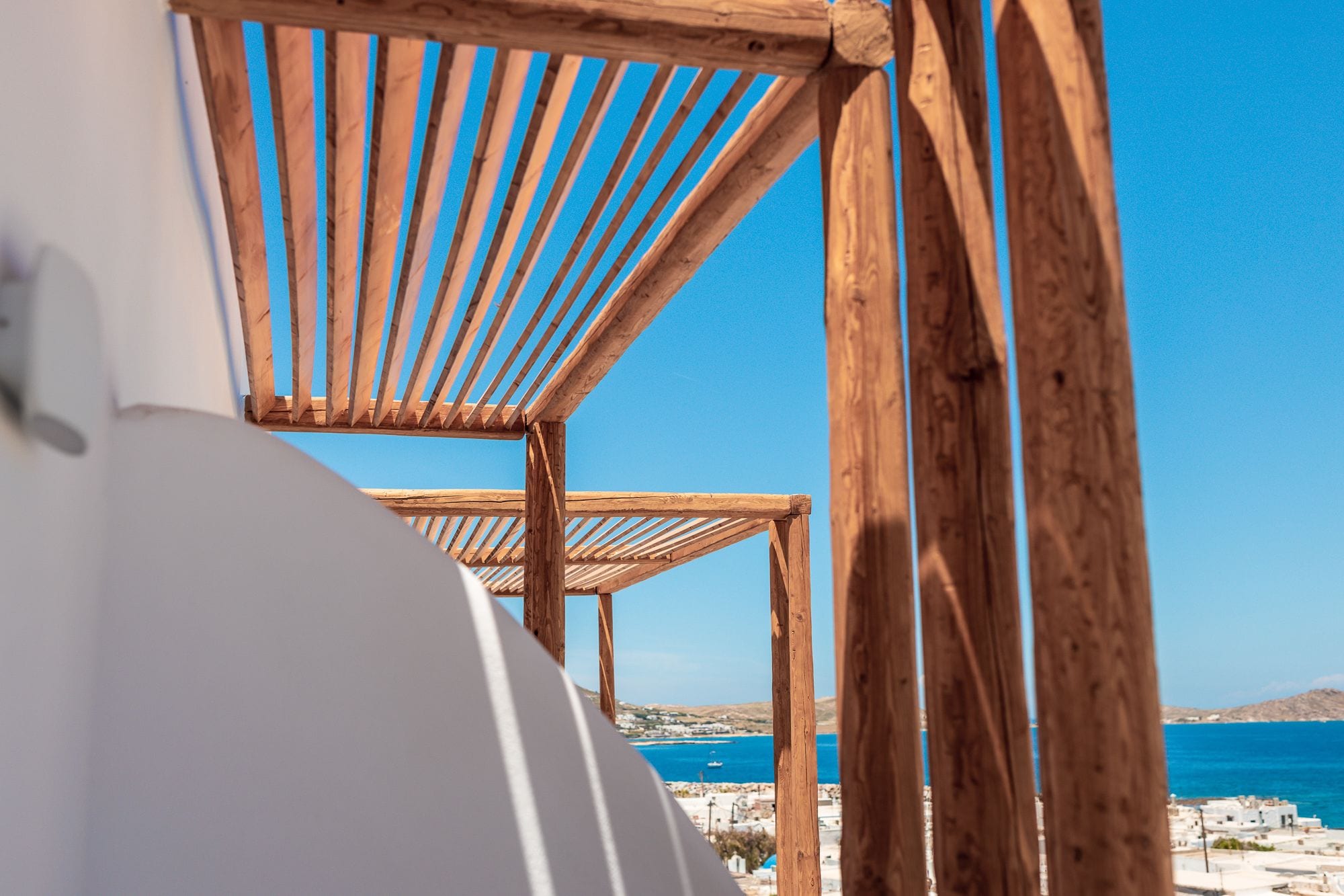 A wooden pergola structure with a clear view of the sea and distant buildings.