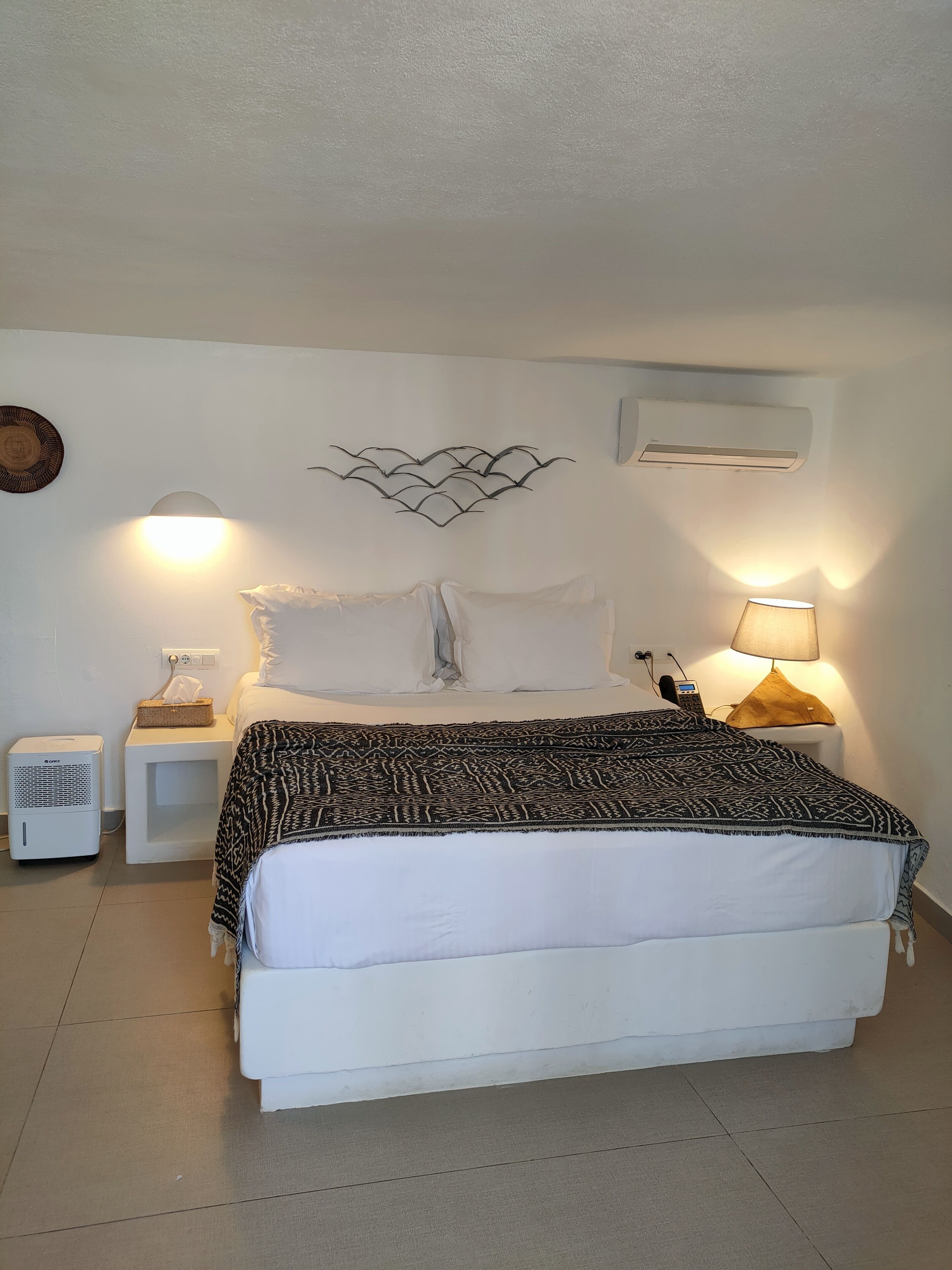 A neatly arranged bedroom with a bed, bedside tables, a wall-mounted air conditioner, and a lamp.