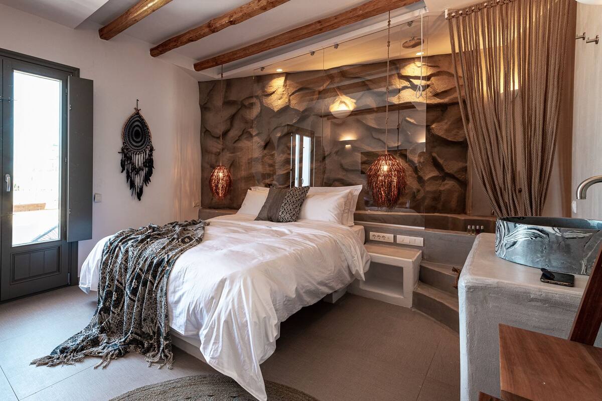 Ein modernes Schlafzimmer mit einem großen Bett, einer Steinwand und einer Pendelleuchte.