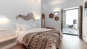 A bedroom with a bed, bedside table, and a bench. There is a window with curtains and a view of the outside. - Bohemian Luxury Boutique Hotel - Adults Only (Paros)