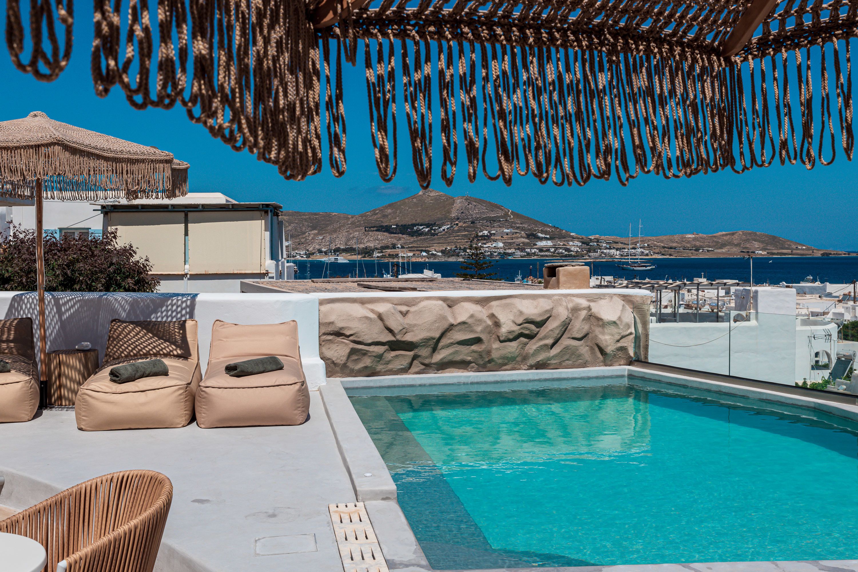 A poolside area with lounge chairs and a view of the sea and a mountain.