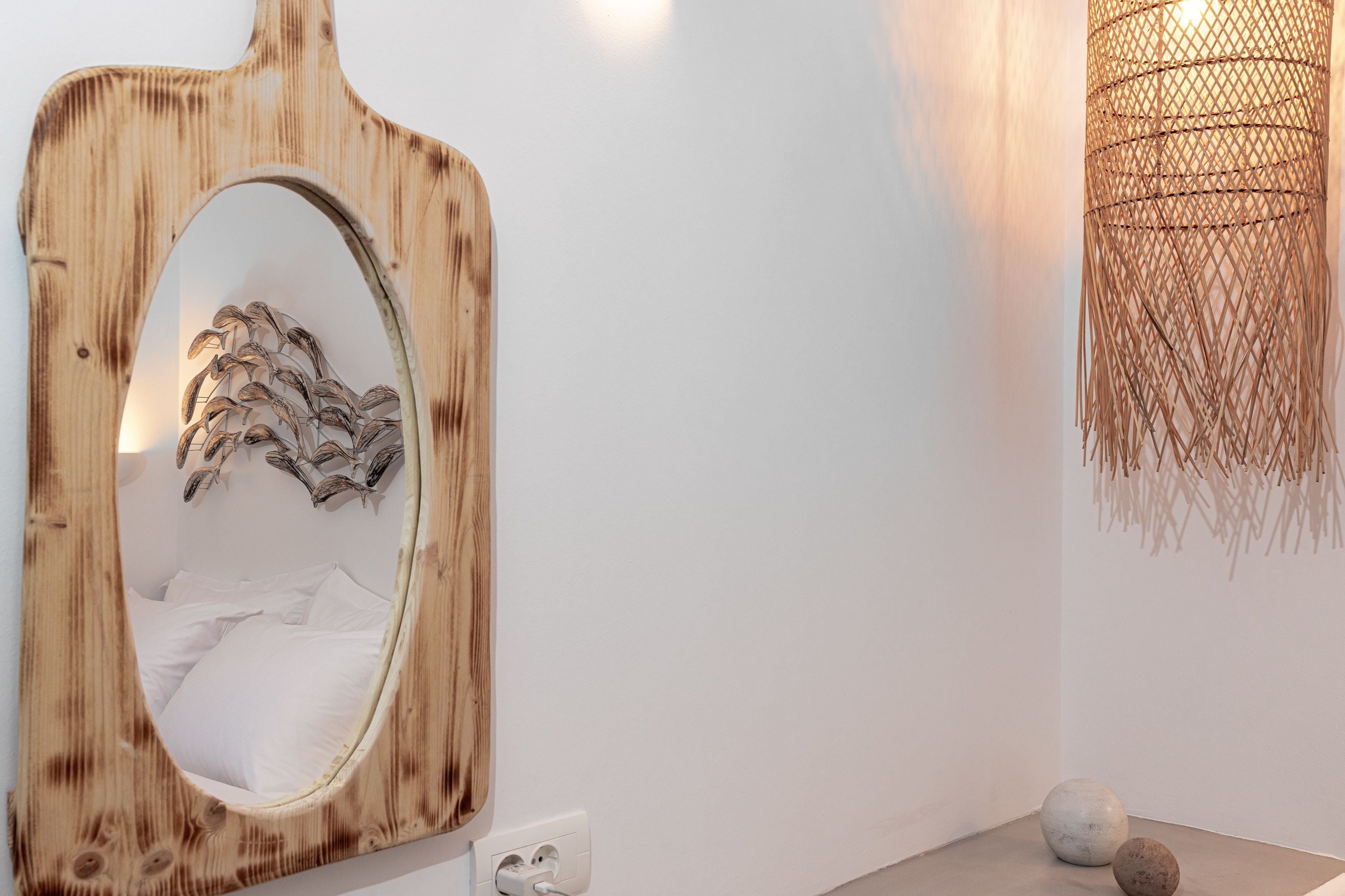 A bathroom with a wooden-framed mirror, a wall-mounted light fixture, and a small table with decorative stones.