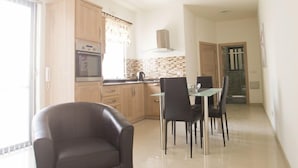 A modern kitchen with a dining area, a sofa, and a glass table. - Waterside Apartments (Zebbug)