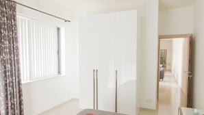 A bedroom with a bed, a ceiling fan, a window with curtains, and a door leading to another room. - Waterside Apartments (Zebbug)
