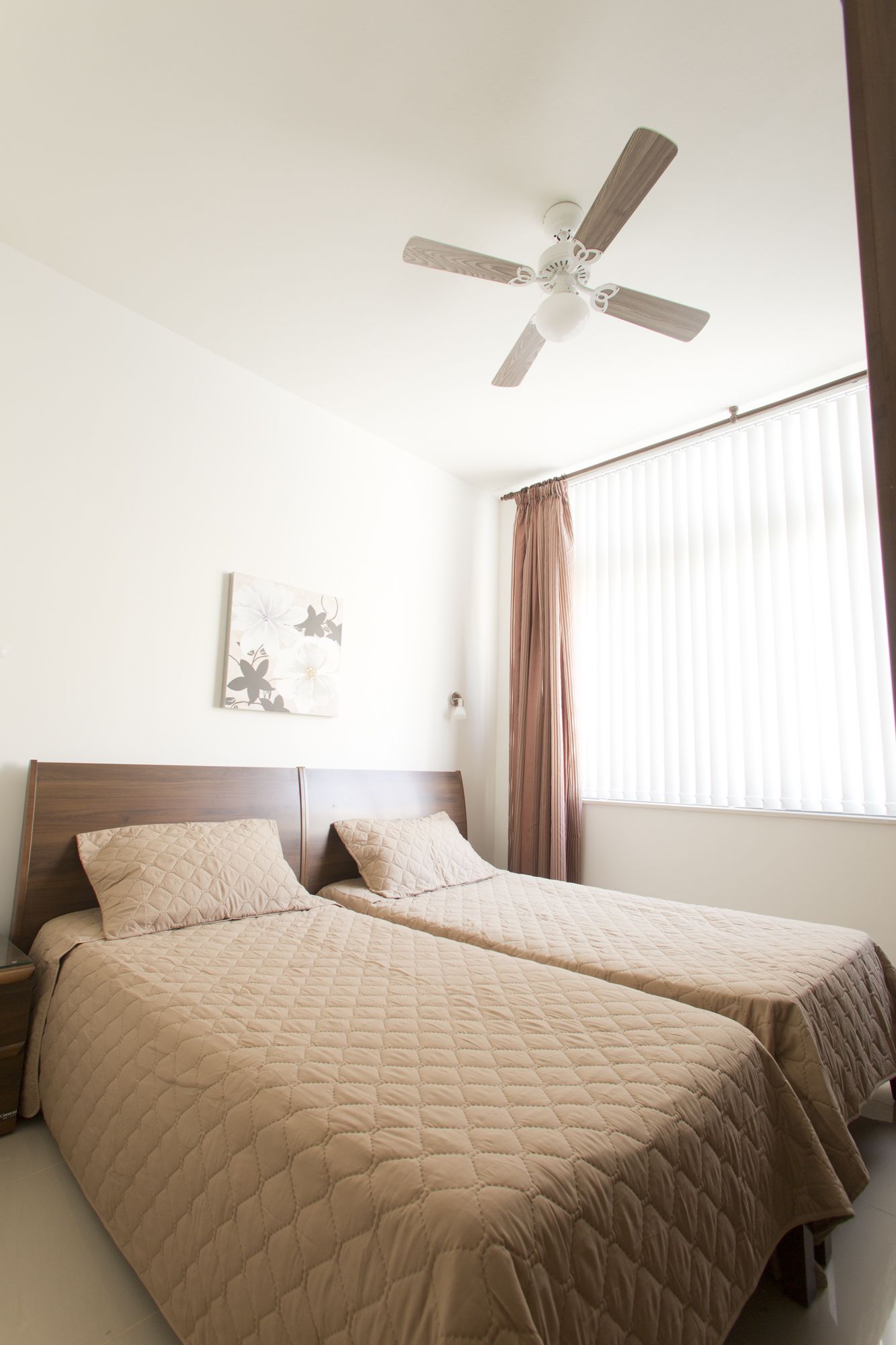 Une chambre d’hôtel avec deux lits, un ventilateur de plafond, une fenêtre avec des stores et un luminaire fixé au mur.