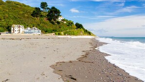 Une plage avec un bâtiment situé sur une colline, un ciel dégagé et des vagues qui se rapprochent du rivage.