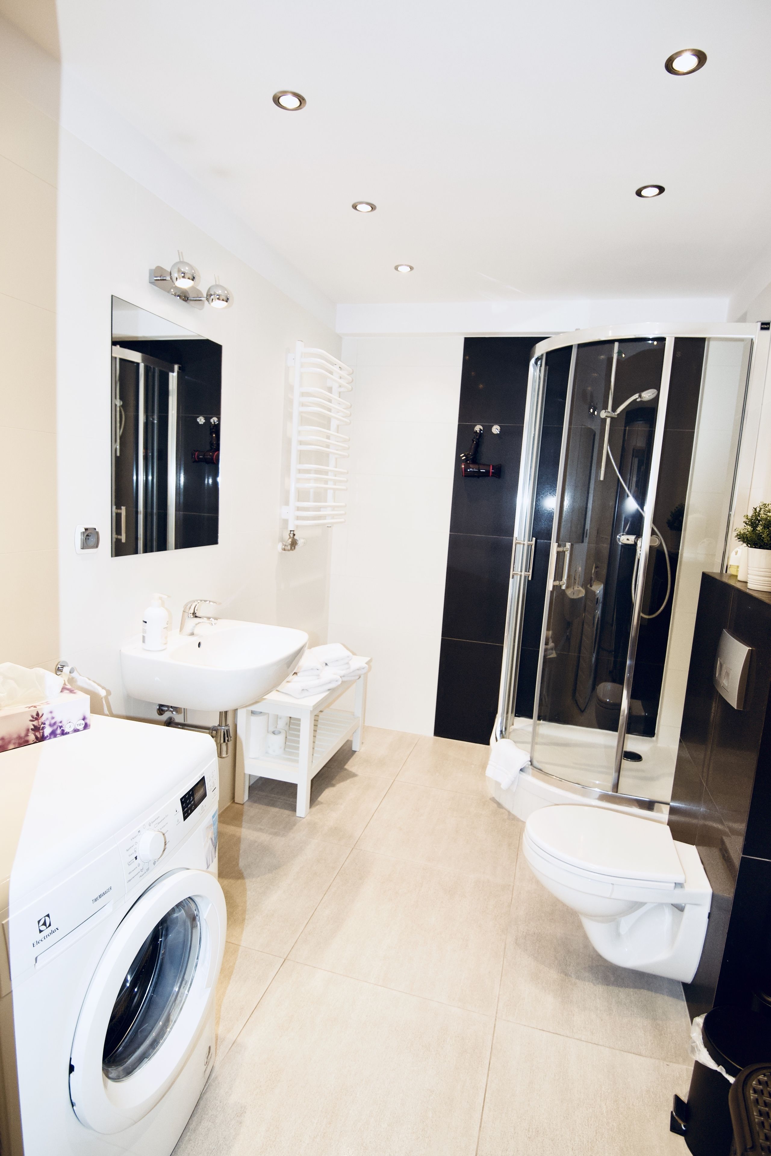 A modern bathroom with a washing machine, a toilet, a sink, and a glass-enclosed shower.