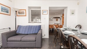En moderne stue med en grå sofa, et spisebord dækket til fire personer, og et køkken i baggrunden.