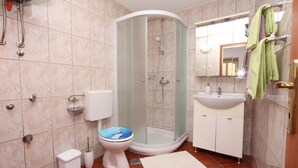 A bathroom with a glass-enclosed shower, a toilet with a blue seat, a sink, and a mirror. - Apartments Olga (Rovinj)