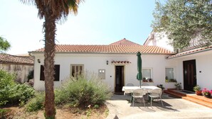 A white building with a tiled roof, a patio with a table and chairs, and potted plants. - Apartments Olga (Rovinj)