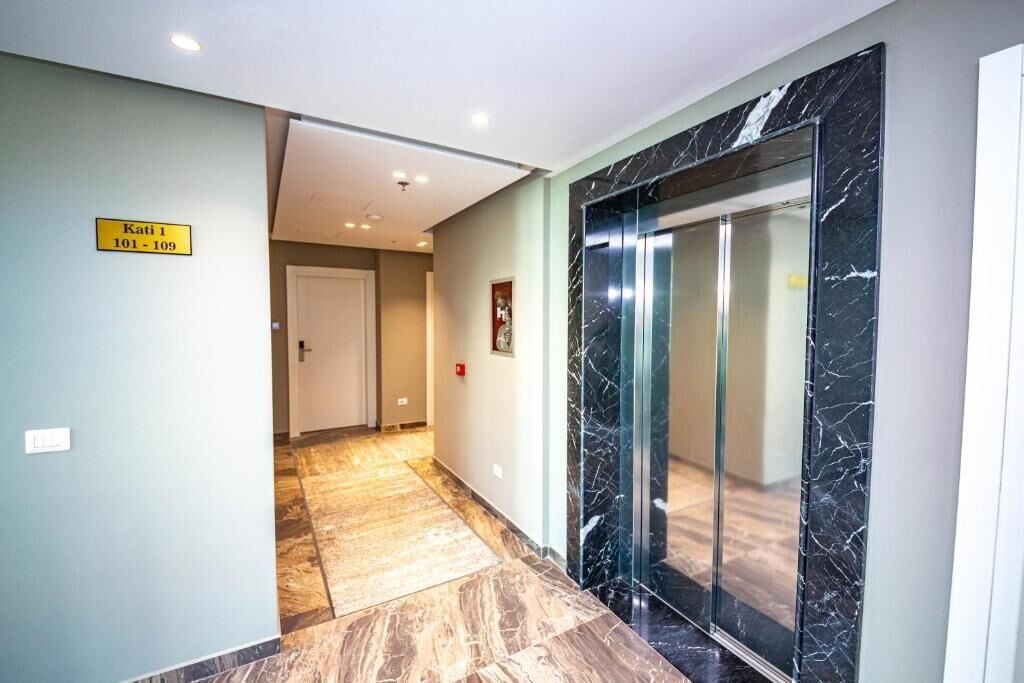 A hallway with a marble floor, a glass elevator, and a sign indicating room numbers 101-109.