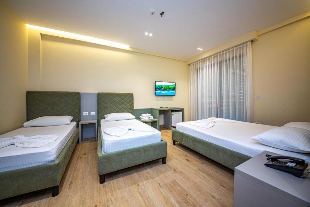 A hotel room with two single beds, a small desk with a chair, a television on the wall, and a window with curtains.