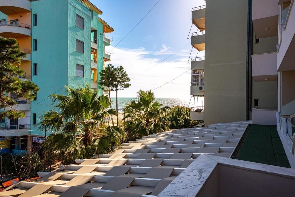 A hotel with a pool area, palm trees, and a view of the sea.