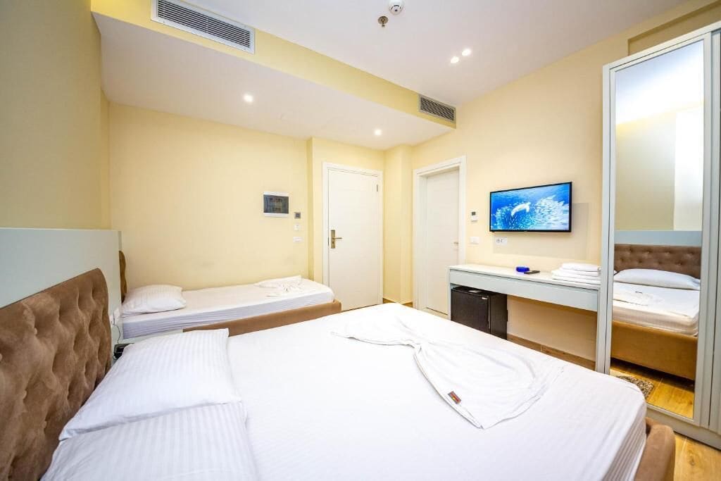 Hotellihuone, jossa on kaksi sänkyä, televisio, peili ja vaatekaappi.