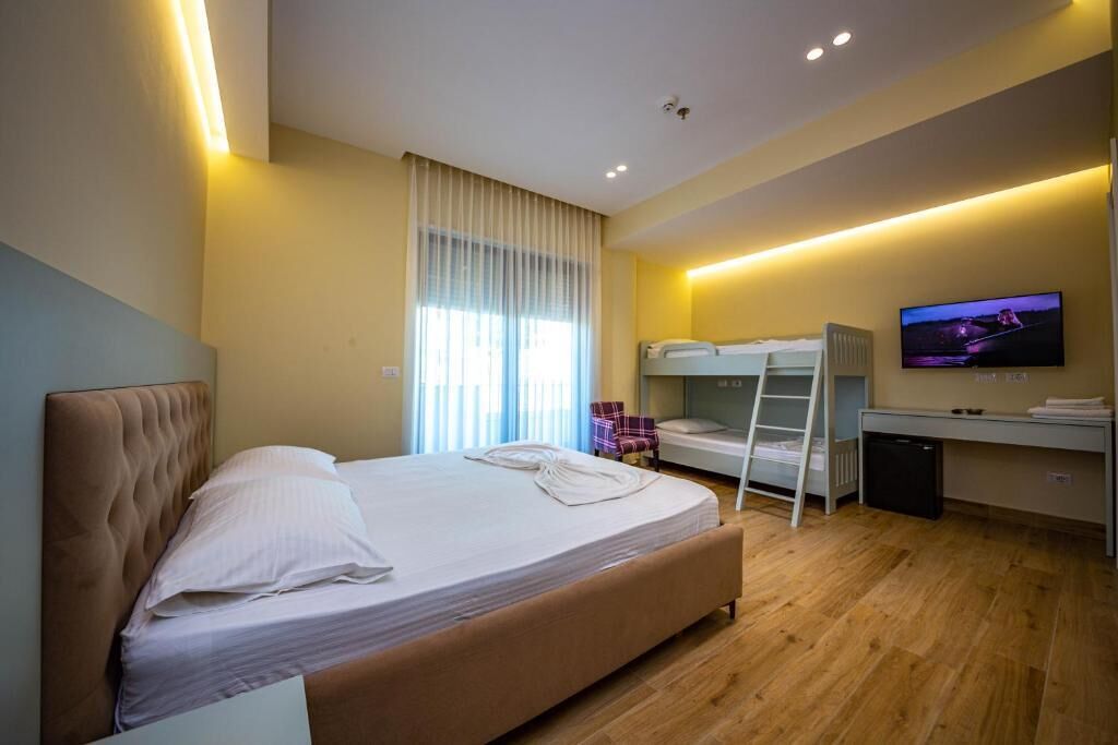 A modern hotel room with a large bed, a desk, a TV, and a bunk bed.