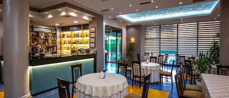A hotel lobby with a bar area, round tables, and chairs.