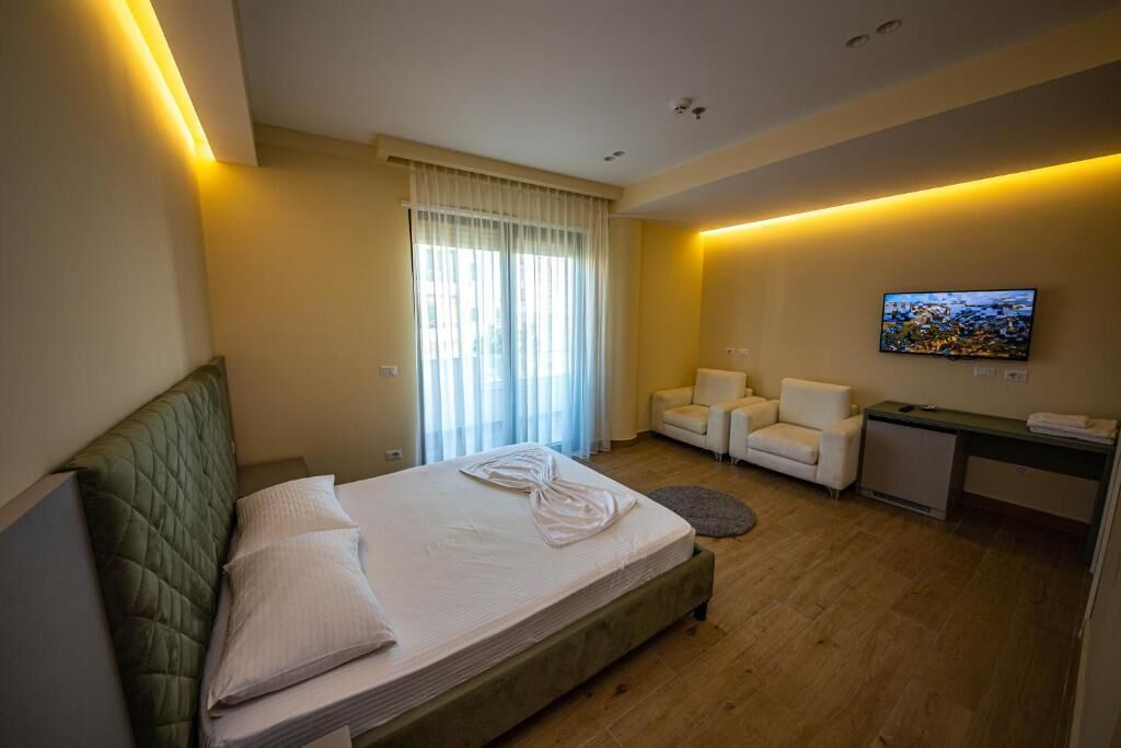 A hotel room with a bed, a desk, a chair, a TV, and a window with curtains.