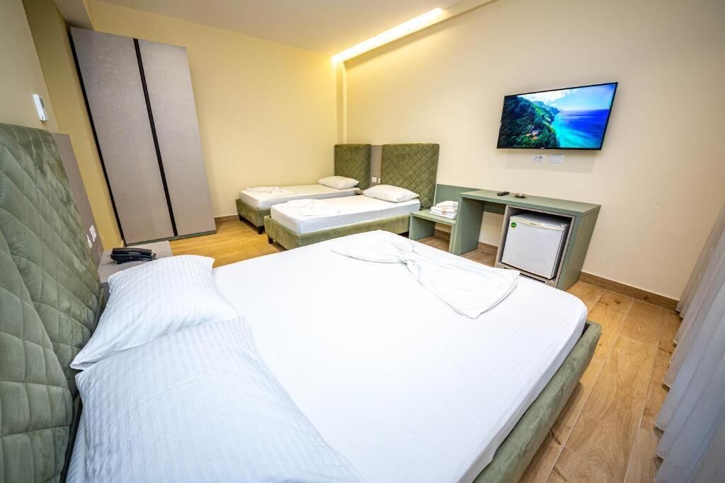 A hotel room with a large bed, two smaller beds, a desk with a computer, and a TV on the wall.