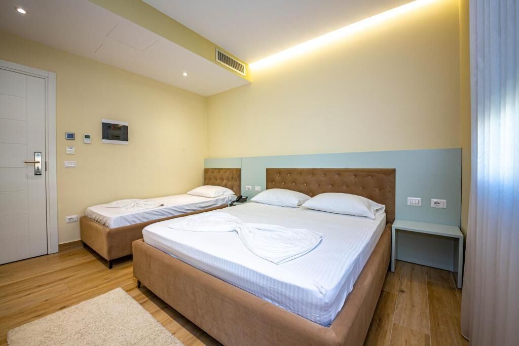 Une chambre d’hôtel avec deux lits, un plancher en bois, une porte blanche et une table de chevet avec une lampe.