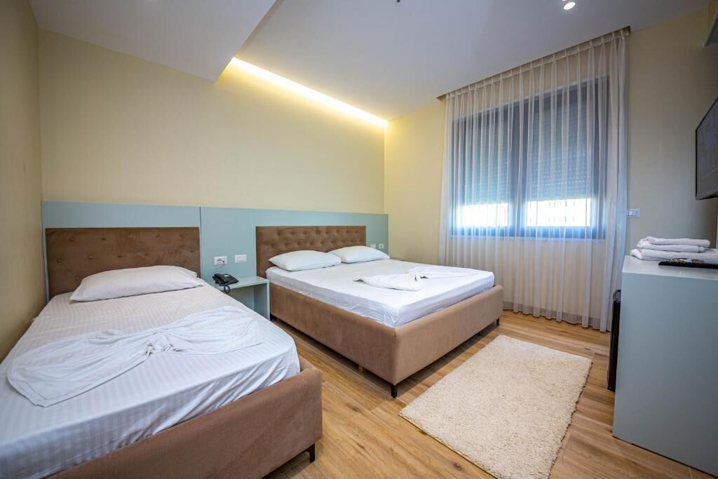 Ein Hotelzimmer mit zwei Betten, einem Schreibtisch und einem großen Fenster mit Vorhängen.
