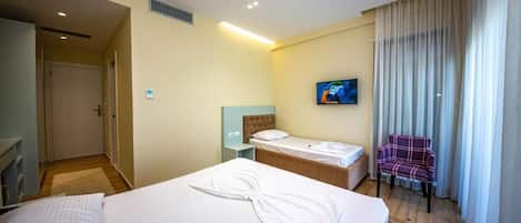Una camera d'albergo con due letti, una televisione a parete e una sedia vicino alla finestra.