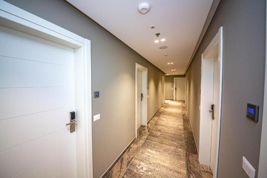 Un couloir d’hôtel avec des portes blanches, un sol en marbre et un éclairage encastré.