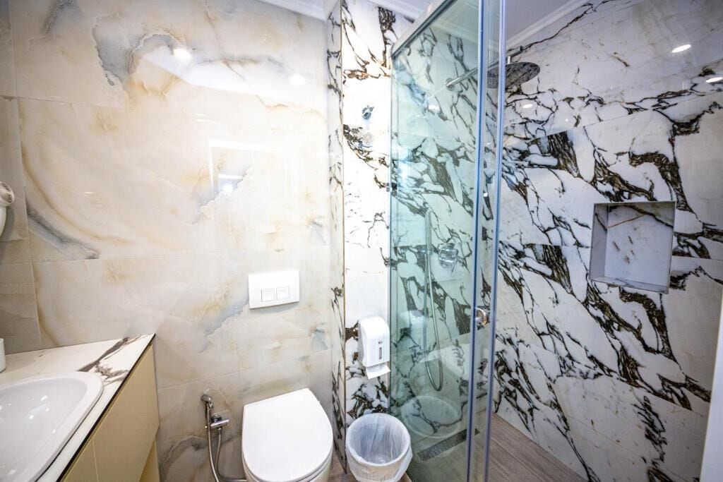 A bathroom with marble walls, a glass shower enclosure, a white toilet, and a sink.