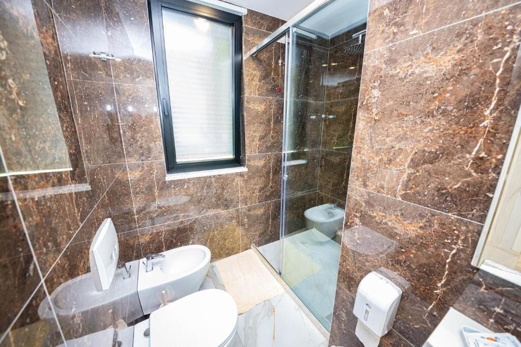 A bathroom with a glass shower enclosure, a toilet, a sink, and a bidet.