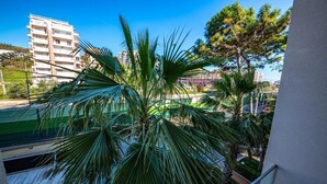 Un balcón con palmeras y vista a un edificio al fondo.