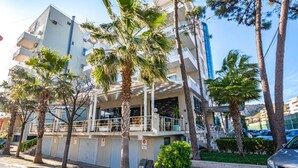 Un hotel de varios pisos con balcones, palmeras y un área de estacionamiento.