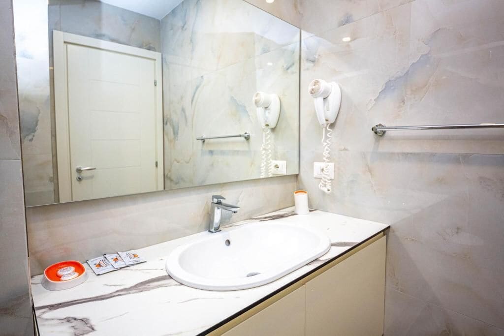 A bathroom with a white sink, a mirror, a hairdryer, and a towel rack.